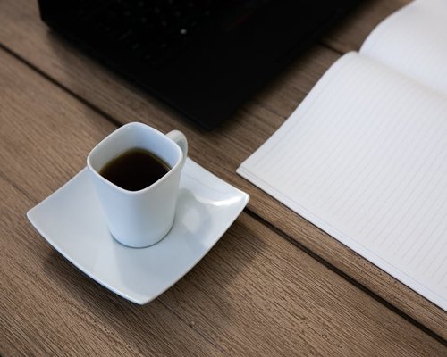 A freshly brewed cup of Colombian black coffee on a tidy office desk next to a notebook